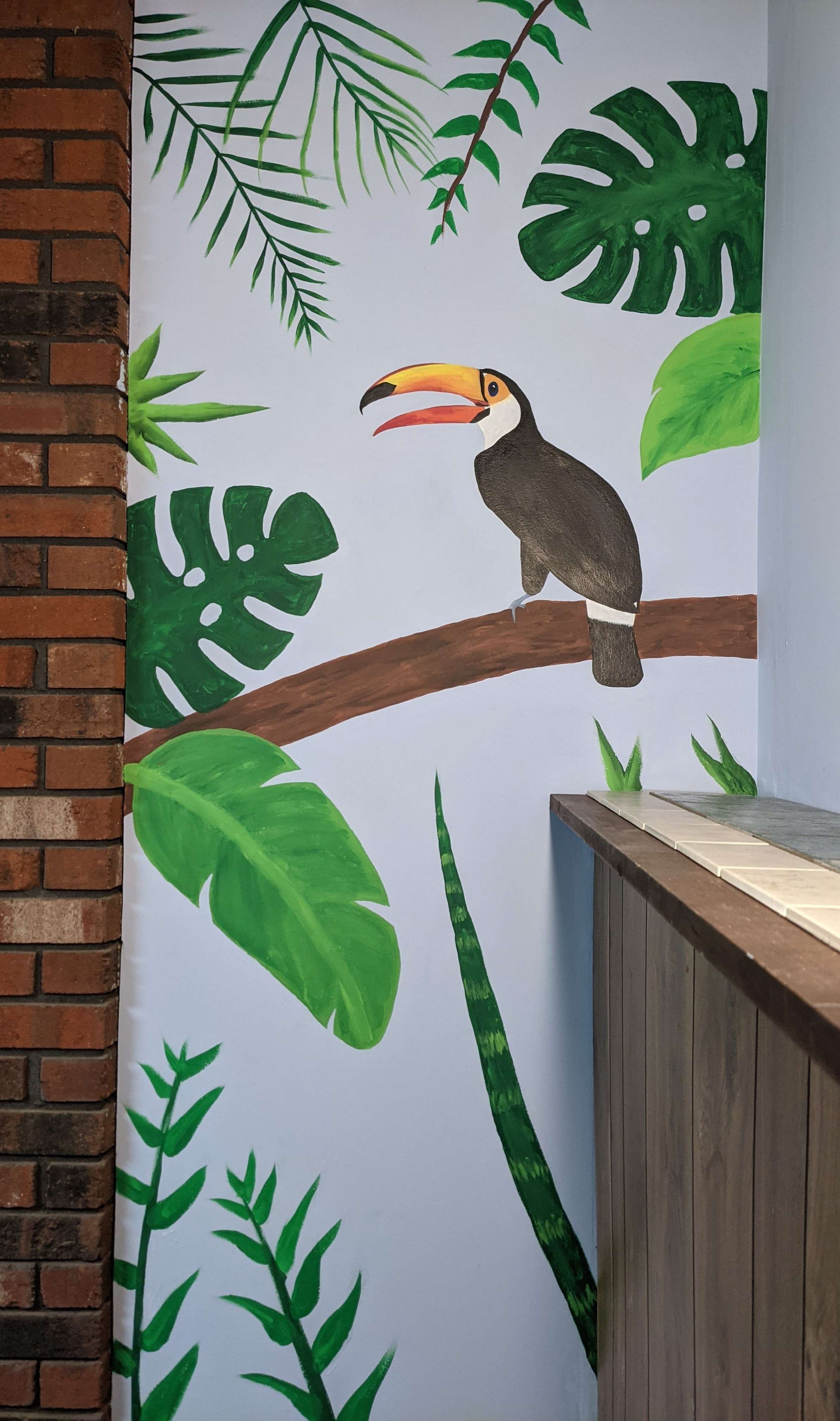 Toucan and tropical foliage mural beside a brick wall